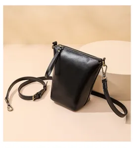 Close-up detail of a minimalist black leather crossbody bag with metal zipper and strap.