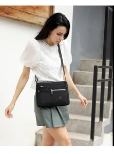 Detail scene view of women black nylon crossbody bag worn by model on outdoor stairs.