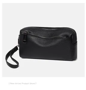 Black genuine leather clutch bag detail shot, pebble grain texture with metal zipper and strap.