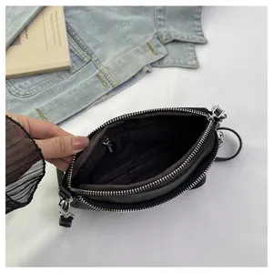 Black leather crossbody bag interior detail showing double zippers, fabric lining and pocket.