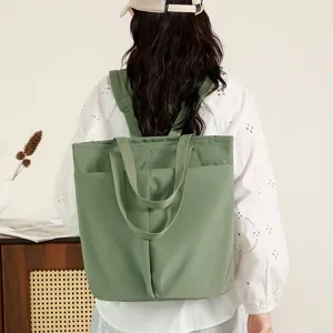 Detail view of a green nylon tote backpack with double handles and front pocket, worn by model.