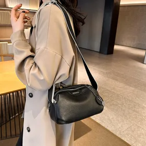 Close-up view of a black genuine leather cross-body bag with wide strap, worn by model.