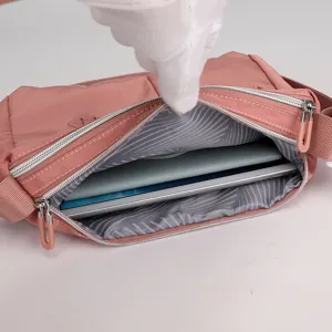 Detailed view of pink nylon crossbody bag interior capacity, showing multiple zippers and lining.