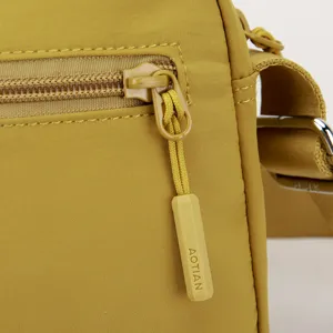 Close-up detail of yellow nylon shoulder bag zipper pull and hardware, minimalist design.
