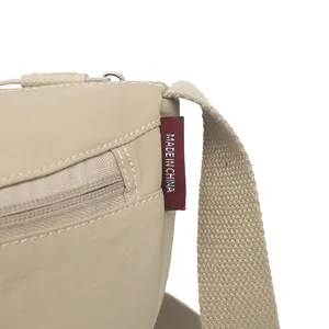 Close-up detail of lightweight waterproof nylon crossbody bag, showing strap seam and red tag.