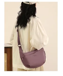 Detail showcase view of a stylish purple nylon dumpling crossbody bag worn by a model.