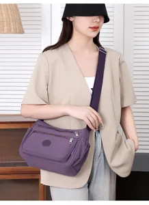 Detailed view of the stylish purple nylon crossbody bag worn by model, showing zipper pockets.