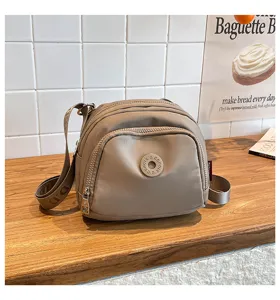 Detail shot of a casual khaki nylon crossbody bag featuring multi-zipper pockets and stylish strap.