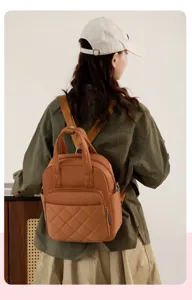 Detail view of a stylish brown quilted nylon backpack worn by a model, featuring top handle.