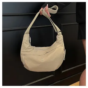 Detail view of beige nylon crescent shoulder bag, featuring wide adjustable strap and zipper.