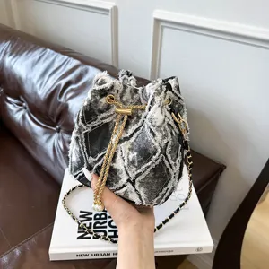 Trendy denim patchwork bucket bag with chic gold chain strap and stylish frayed fringe details.