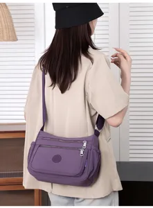 Detail view of the purple nylon multi-pocket crossbody bag with adjustable strap and zippers.