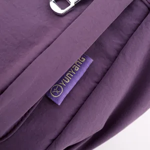 Nylon crossbody bag detail view showing durable purple fabric, metal zipper, and brand label.
