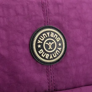 Detalle de tela de mochila de nylon purpura con parche de logo redondo y costuras limpias.