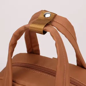 Detailed view of brown nylon backpack handle and metal snap button, durable casual bag.