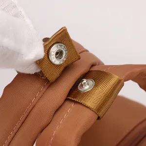 Close-up detail of brown nylon backpack strap featuring durable metal snap button and fine stitching.