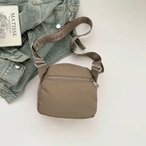 Khaki nylon crossbody bag with zipper front pocket and stylish woven strap detail.