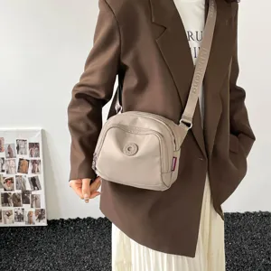 Casual nylon crossbody bag detail view showing khaki fabric, wide strap and round logo.