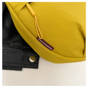 Close-up detail of yellow nylon crossbody bag with zipper pull and branded woven label.