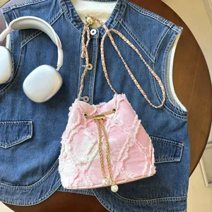 Detail view of pink frayed denim bucket bag with gold chain strap and pearl drawstring.