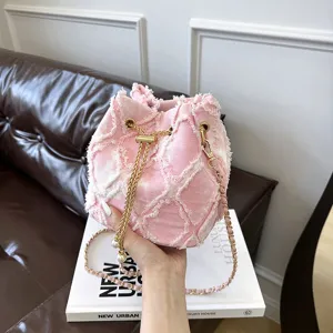 Pink denim bucket bag detail shot showcasing quilted embroidery and chic golden chain strap.