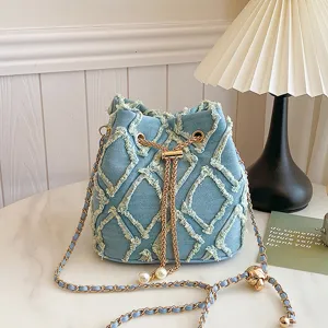 Detailed view of stylish light blue denim bucket bag with frayed diamond pattern and chains.