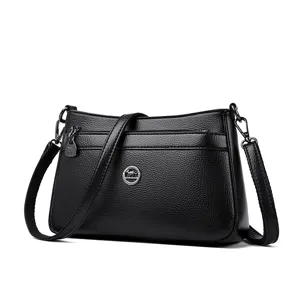Detailed view of black leather shoulder bag with metal logo, zipper pocket and strap.