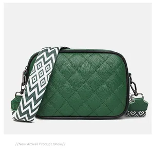 Close-up of green quilted leather crossbody bag with wide geometric strap and metal hardware.