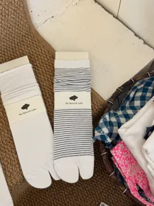 Detailed view of casual split-toe tabi socks in white and striped styles with paper packaging.