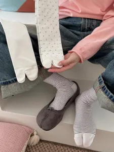 Close-up detail shot of stylish split-toe socks paired with minimalist flats and denim jeans.