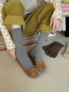 Detailed view of grey ribbed split toe crew socks paired with brown tabi flats indoors.