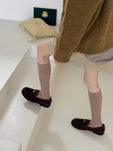 Detail shot of brown ribbed knit calf socks worn with loafers in a minimalist room setting.