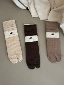 Detail view of solid color split-toe slouch socks in beige, dark brown, and light brown hues.