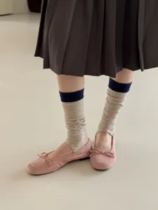 Close up detail shot of striped stirrup socks paired with pink flat shoes and pleated skirt.