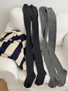 Close-up view of warm knit tights in dark and medium grey, styled neatly on a white sofa.