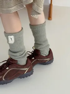 Close-up detail of grey ribbed knit wool socks with patch tag, cozy winter leg warmers style.