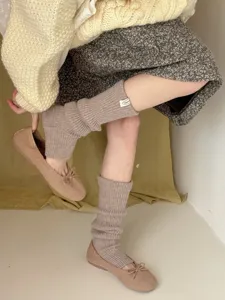 Close-up view of cozy knit leg warmers in neutral beige, styled with matching flats and skirt.