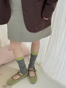 Detail view of women striped stirrup socks paired with green shoes and skirt in lifestyle setting.