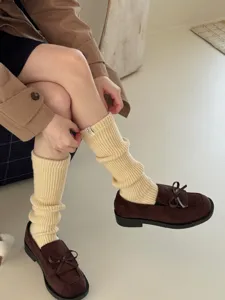 Close-up of cozy beige knitted leg warmers paired with brown loafers for winter warmth.