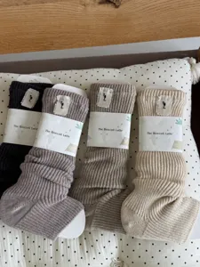 Detailed closeup of soft knitted slouch socks in four neutral colors with paper packaging.