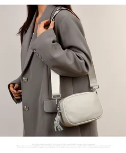 Detail view of a stylish leather crossbody bag with wide strap and chic tassel accent.