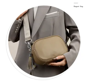 Leather crossbody camera bag detail showing texture, wide strap and chic tassel pendant.