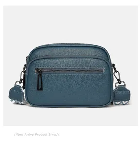 Détail du sac bandoulière en cuir bleu, avec double fermeture éclair et large sangle.