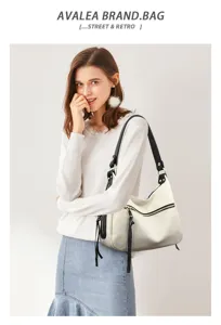 Detailed view of white hobo shoulder bag with black straps, metal zippers, and chic tassels.