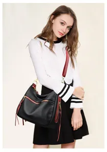 Detail view of a stylish black women's crossbody shoulder bag with red trim and tassels.
