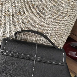Gros plan sur le sac à main en cuir noir avec coutures blanches et poignée solide.