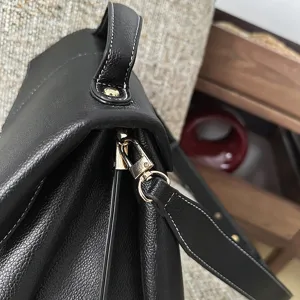 Gros-plan sur le sac à main pour femme en cuir noir avec coutures blanches et détails dorés.