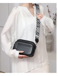 Sac bandoulière en cuir noir avec sangle large à motifs et double fermeture éclair.