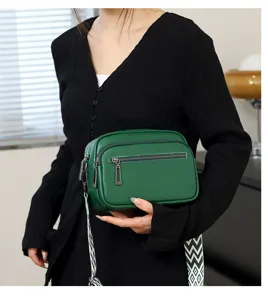 Sac bandoulière en cuir vert pour femme avec double fermeture éclair et large sangle à motifs.