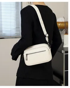 Vue rapprochée du détail du sac bandoulière en cuir blanc avec large sangle géométrique.